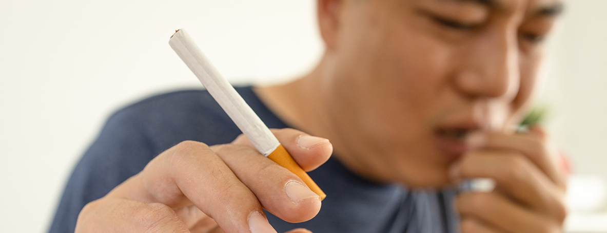 Homem segurando um cigarro e tossindo, sofrendo com os malefícios do cigarro